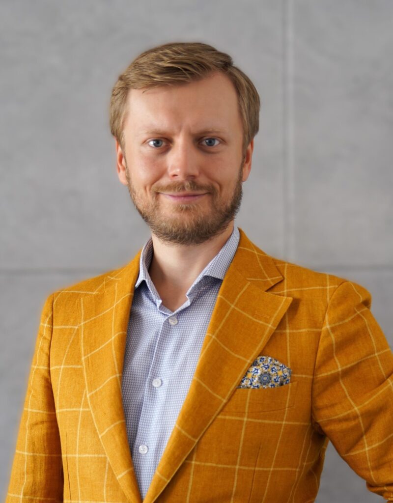 Młody mężczyzna uśmiechnięty w zółtej marynarce.