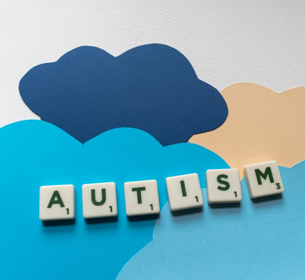 Scrabble tiles spelling 'Autism' on colorful paper clouds, promoting autism awareness creatively.